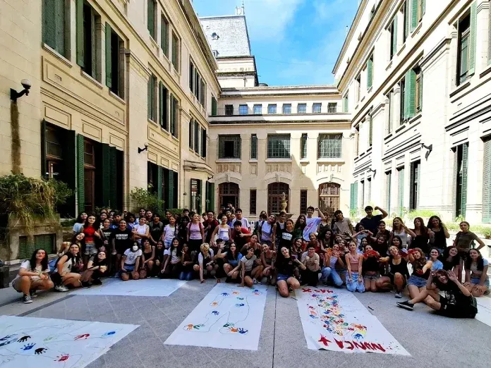 Estudiantes posan en el patio del colegio junto a telas blancas con siluetas y manos pintadas de colores.